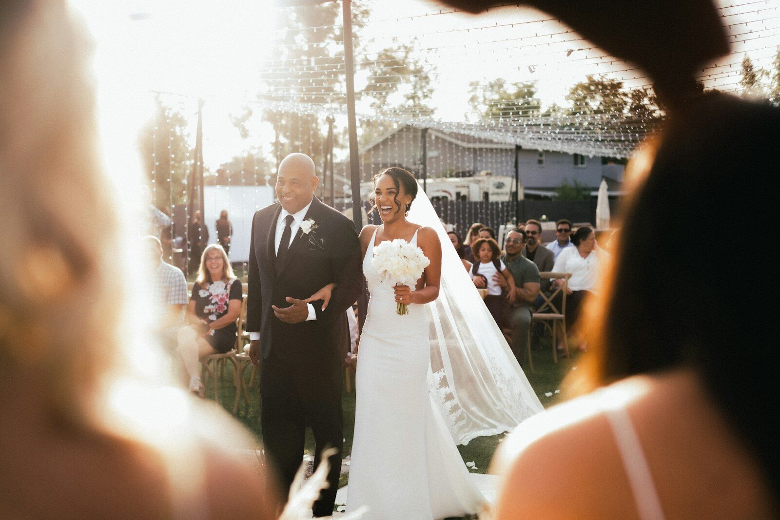 Une mariée remonte l'allée au bras d'un proche lors d'une cérémonie en plein air